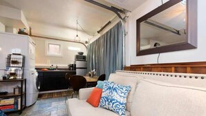 A compact living space with a kitchenette, a sofa with patterned cushions, and a large mirror on the wall. - #StayinMyDistrict Hyde Park Northend Studio (Boise)