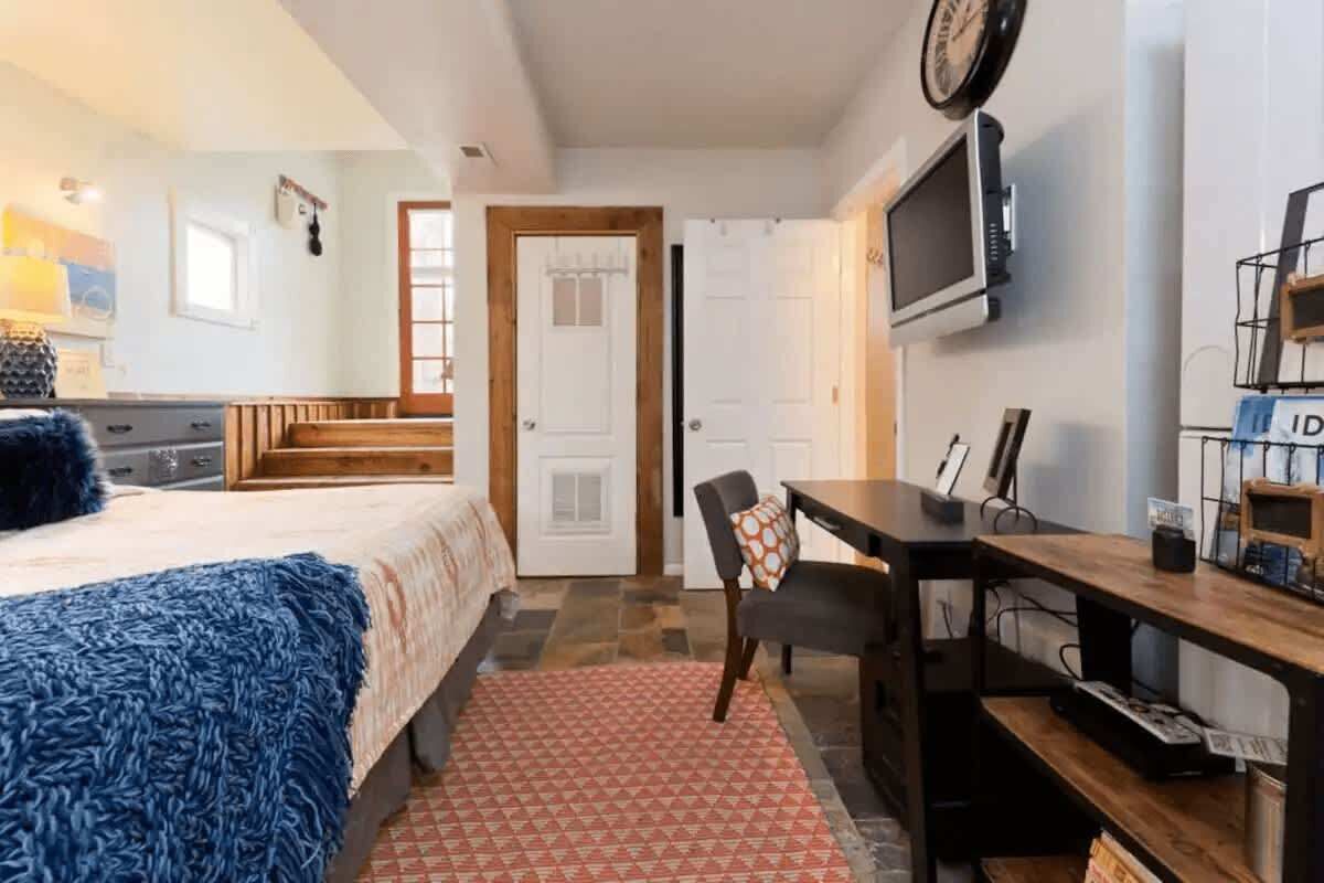 A bedroom with a bed, a desk, a chair, a TV, and a door.