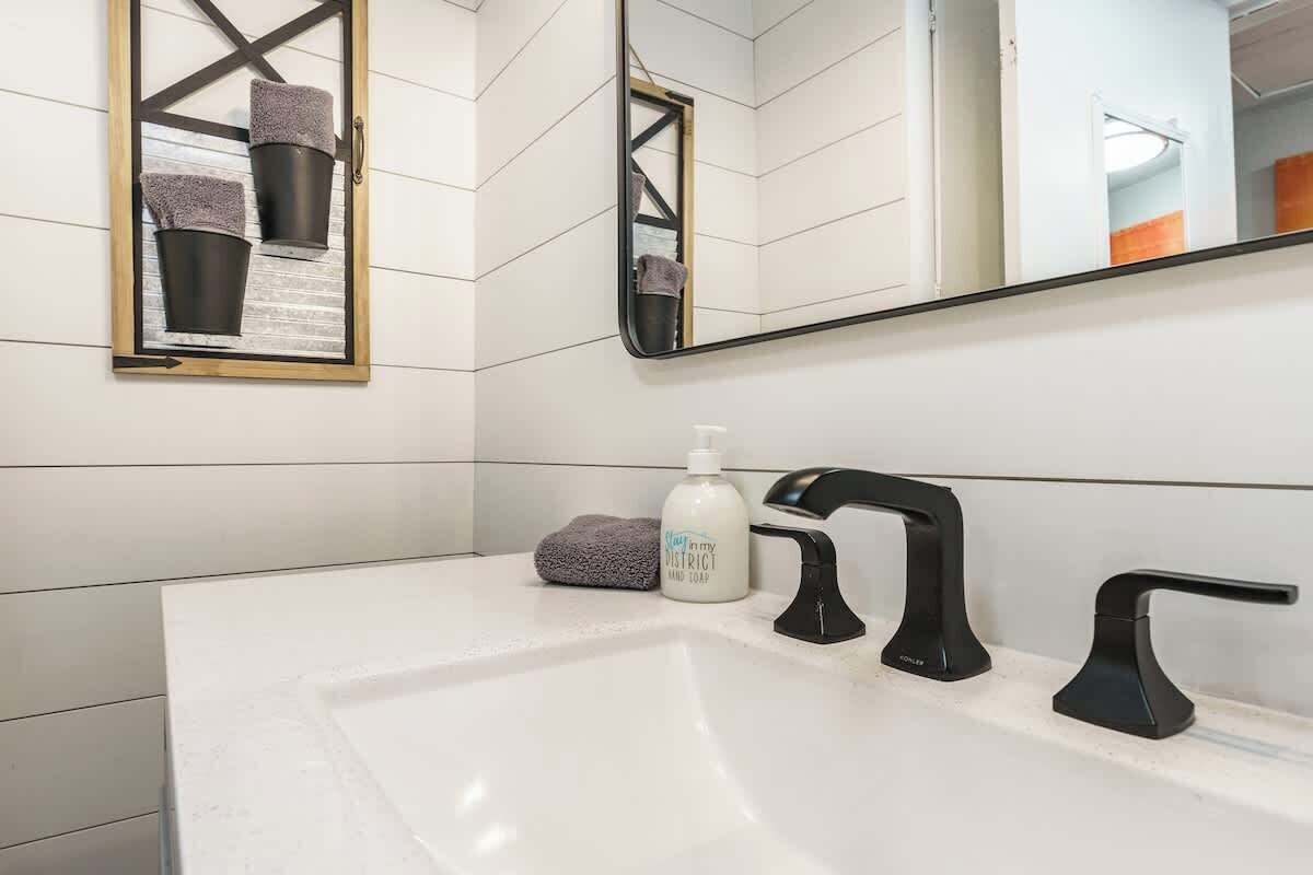 Un baño moderno con un lavamanos blanco, grifos negros y un espejo con marco dorado.