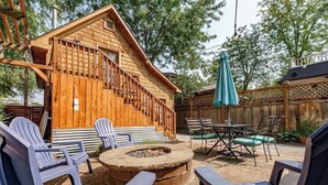 Una cabaña de madera con terraza, asientos exteriores y un pozo de fuego.