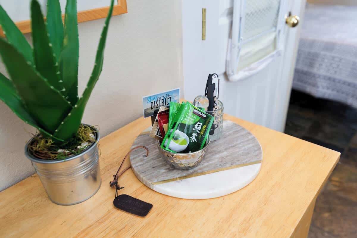 Une petite table sur laquelle se trouve une plante en pot, un récipient en métal avec une carte, et une paire de lunettes.