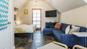 Een slaapkamer met een bed, een bank, een televisie en een raam met zonwering.