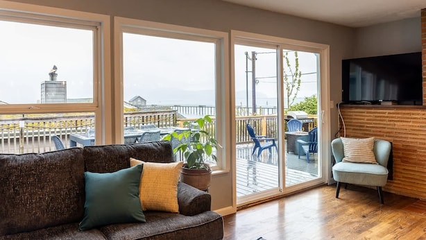 A spacious balcony with a view of the sea, a comfortable seating area with a sofa and chairs, and a flat-screen TV mounted on the wall. - #StayInMyDistrict Garibaldi Bay Views (Garibaldi)