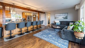 A modern kitchen with bar stools, a dining area with a sofa, and a large window. - #StayInMyDistrict Garibaldi Bay Views (Garibaldi)