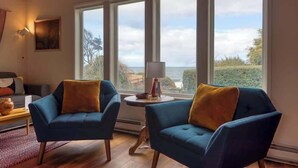 A room with two blue armchairs, a small table with a lamp, and large windows offering a view of the sea. - #StayinMyDistrict Cape Arago Studio Suite (Coos Bay)