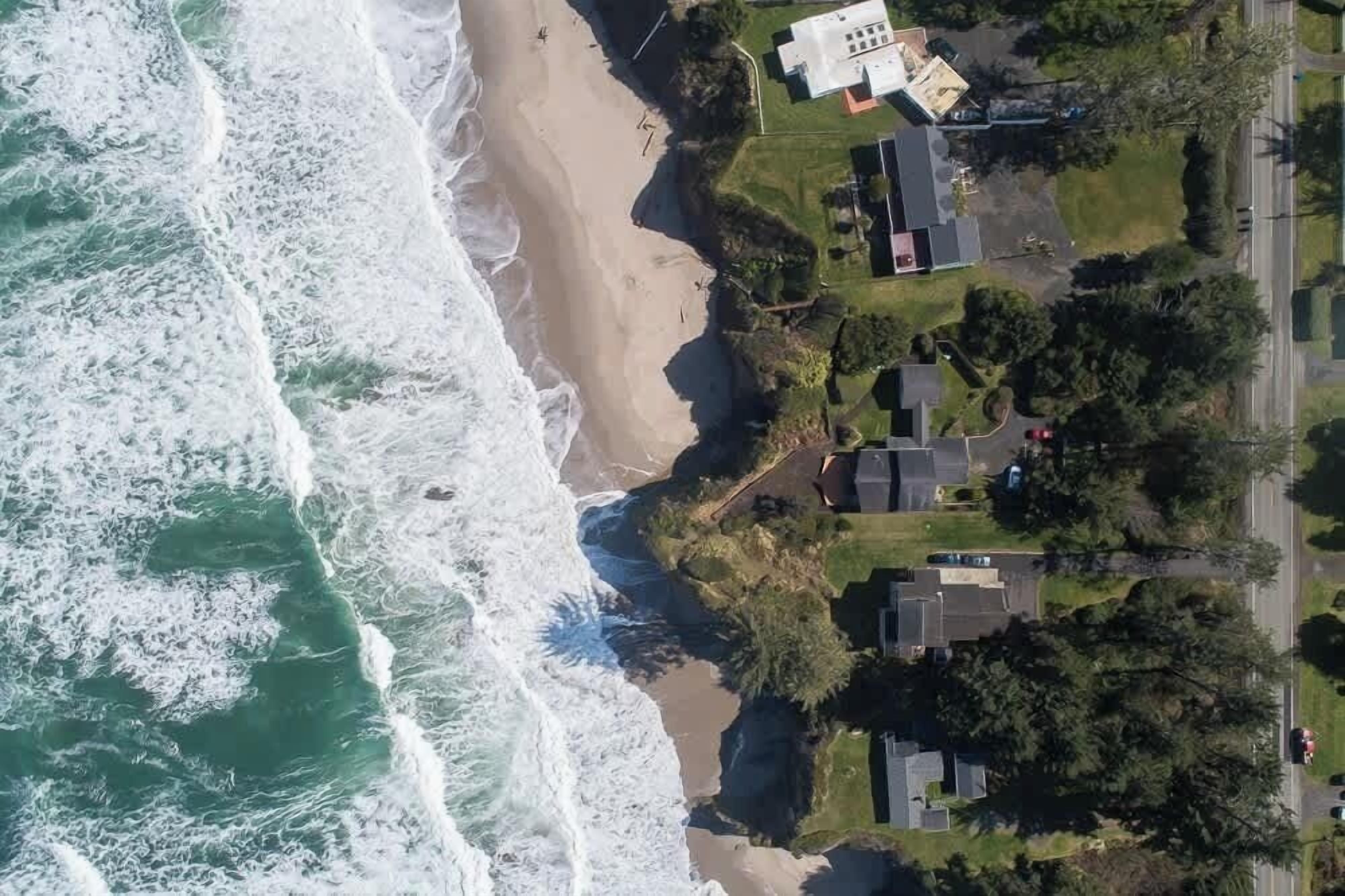 Vue aérienne d’une zone résidentielle côtière, avec des maisons, une plage et une route.