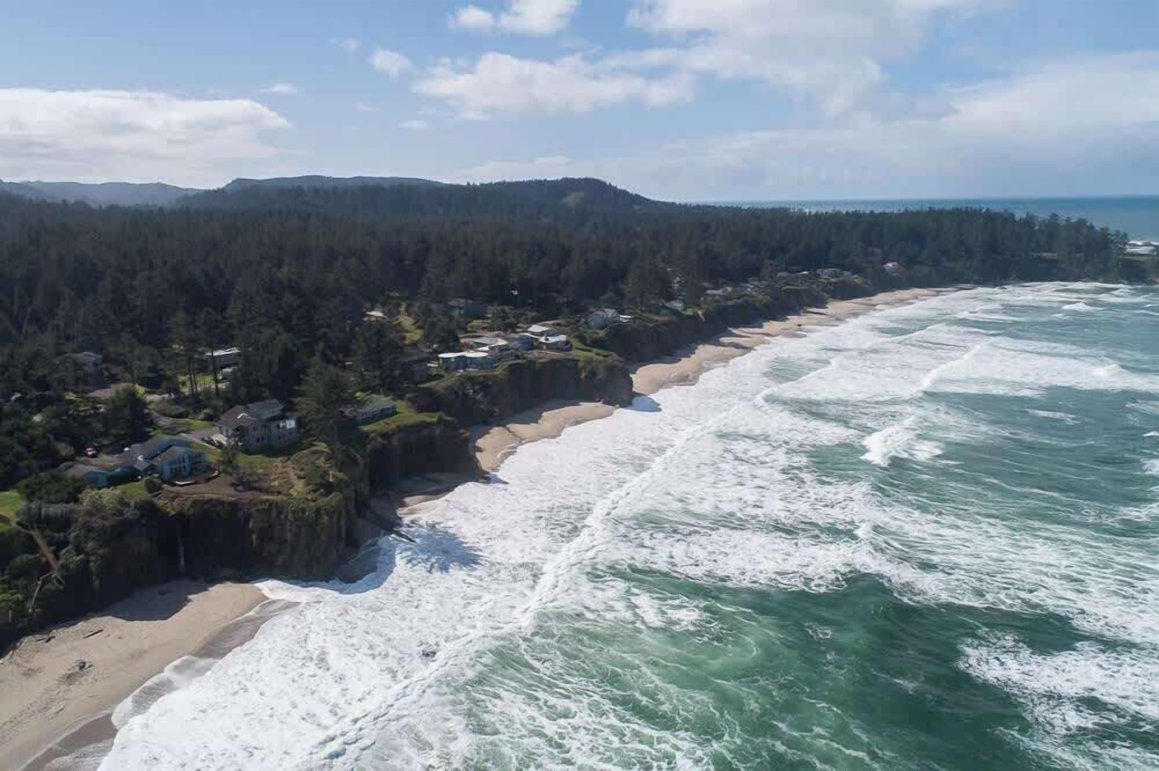 Une zone côtière comprenant une plage, des vagues et une colline boisée.