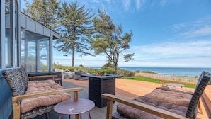 Een terras met zitplaatsen buiten, een vuurkorf en uitzicht op de oceaan.