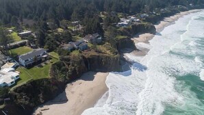 Luchtbeeld van een kustgebied met woningen, een strand en een beboste heuvel.