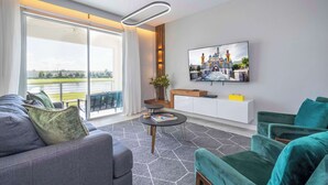 Ein modernes Wohnzimmer mit einer Couch, einem grünen Sessel, einem runden Couchtisch und einem an der Wand befestigten Fernseher.