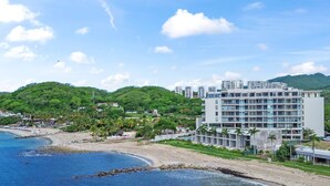 Ein Küstenhotel mit mehreren Stockwerken, einem Strand und üppiger Bepflanzung.