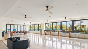 Ein geräumiger, moderner Konferenzraum mit großen Fenstern, mehreren Deckenventilatoren und unterschiedlichen Sitzmöglichkeiten.