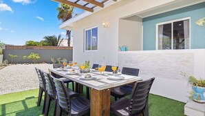 An outdoor dining area with a table set for four, surrounded by chairs, under a wooden pergola.