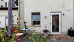 Un patio con plantas en macetas, una mesita y una silla.