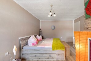 A bedroom with a wooden bed, a bedside table, a lamp, and a wall clock.