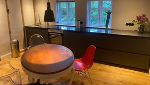 A modern kitchen with wooden beams, a dining table with chairs, and a window with a view of greenery.