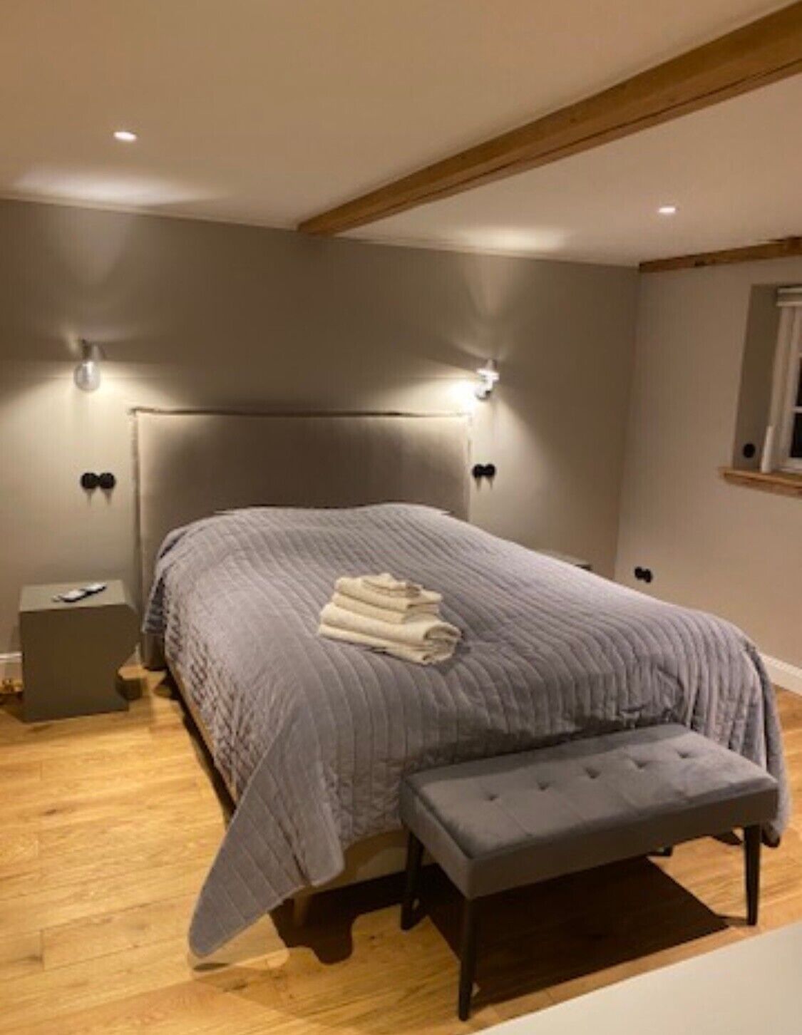 A bedroom with a large bed, bedside tables, a bench, and wall-mounted lights.