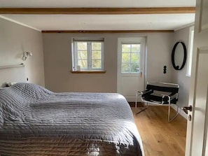 Un dormitorio con cama, dos ventanas, una puerta y una lámpara fijada a la pared.