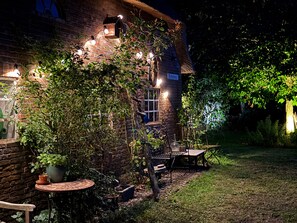 A brick building with a thatched roof, outdoor seating, and string lights.