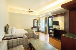 Habitación de hotel con cama, dos sofás, una mesita, televisión y espejo.
