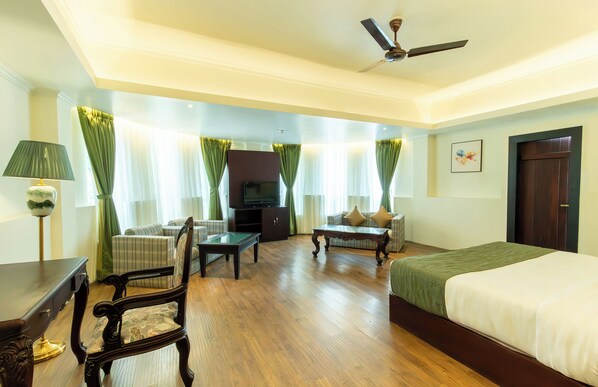 A hotel room with a bed, a sofa, a TV, a desk, and a ceiling fan. - Udaan Keepsa Hotel & Spa Gangtok (Gangtok)