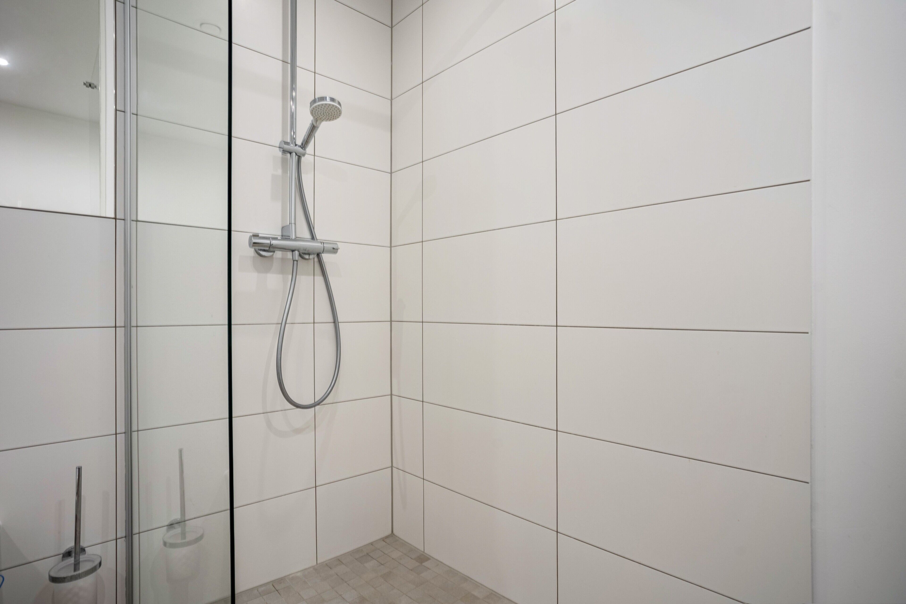 Una ducha con puerta de cristal, cabezal de ducha manual y grifo empotrado.