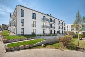 Un moderno edificio residencial de varios pisos, con balcones, un camino pavimentado y un césped bien cuidado.