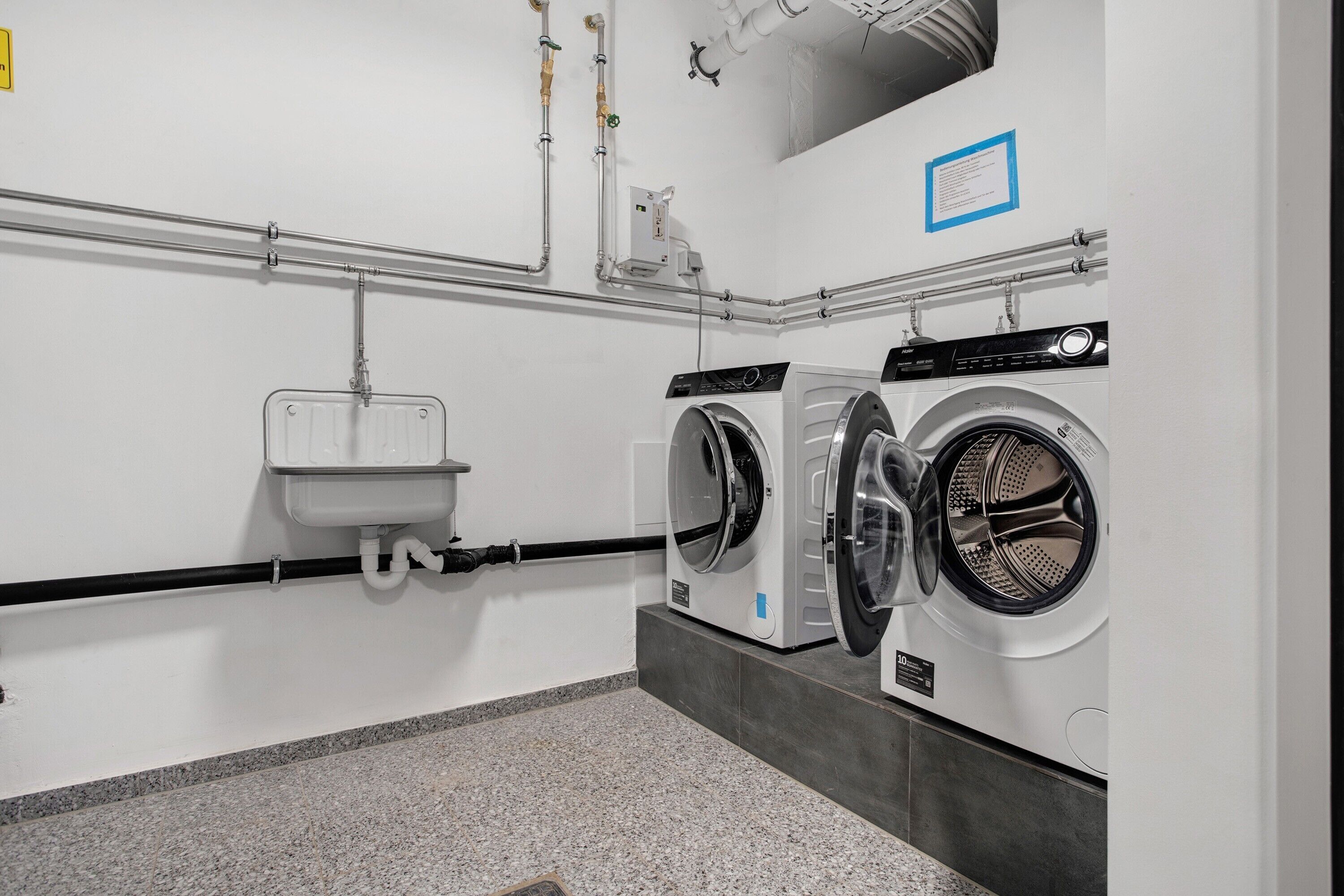 Une buanderie équipée de deux machines à laver, d’un évier et d’un sèche-mains.