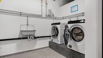 A laundry facility with two washing machines, a sink, and a hand dryer.
