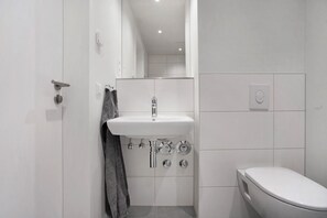 Un baño moderno con un lavamanos blanco, un inodoro y una zona de ducha.