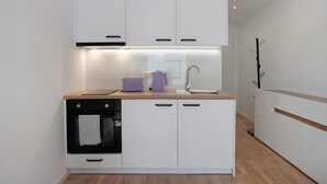 Een kleine keuken met witte kastjes, een houten aanrechtblad, een inbouwoven en een spoelbak.