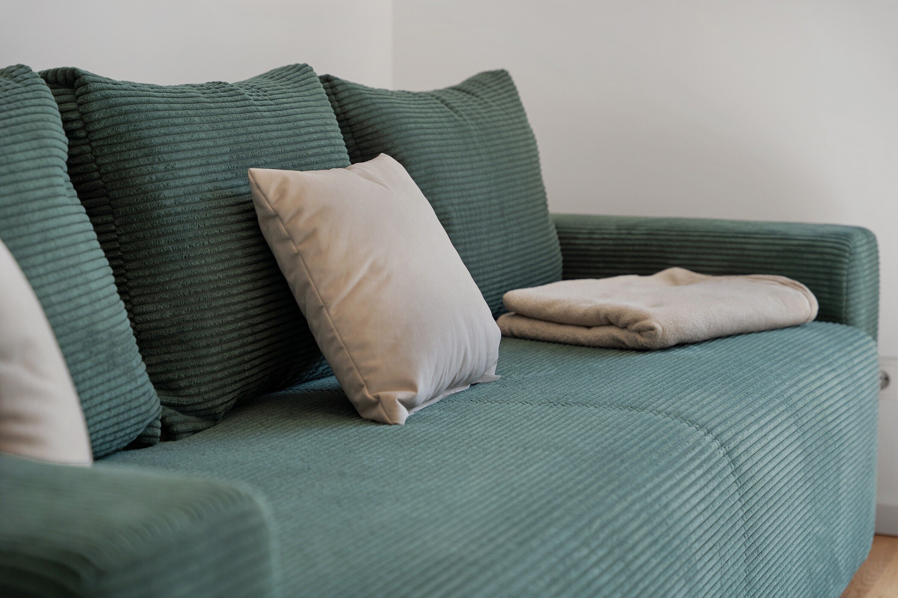 A green sofa with multiple cushions and a folded blanket.