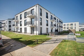 Un edifici residencial modern d'àmbit vertical, amb balcons, un passeig pavimentat i una zona enjardinada.