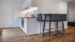 A modern kitchen with a central island, two bar stools, and a dining area with a sofa.