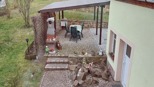 A covered patio area with a table and chairs, a stone pathway, and a small garden with plants and decorative items. - Apartment 'Giesis Wohlfühloase' with Shared Terrace, Private Garden and Wi-Fi (Döbeln)