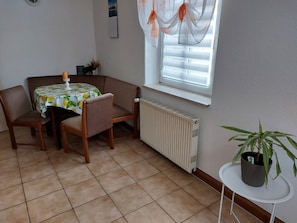 Una habitación con una mesa de comedor, sillas, un radiador, una ventana con cortinas y una planta en maceta.