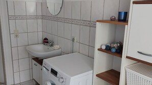 Een kleine wasruimte met een wasmachine, een wastafel en een plank met toiletartikelen.