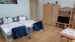 Een slaapkamer met twee bedden, een kledingkast, een tv-meubel en een klein tafeltje.