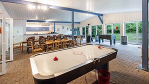 Ein Billardtisch mit Sitzgelegenheiten ringsherum und ein Pool in einem Raum mit hoher Decke und großen Fenstern.