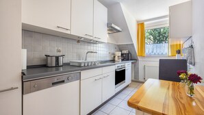 Una cucina moderna con mobili bianchi, una lavastoviglie in acciaio inossidabile, forno integrato e un tavolo da pranzo in legno con un vaso di fiori.