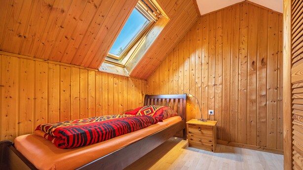 Una stanza con rivestimenti in legno, un letto, un comodino e un lucernario.