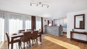 A dining area with a wooden table and chairs, a kitchen with a stone island, and a large mirror on the wall. - Holiday Apartment 5 with Private Terrace, Private Garden and Wi-Fi (Mardorf)