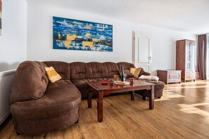 Un salon avec un canapé d’angle marron, une table basse en bois et un tableau abstrait bleu accroché au mur.