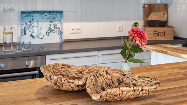 A kitchen with a wooden countertop, woven baskets, a vase with a flower, and a 'Brot' bread box. - Holiday Apartment 5 with Private Terrace, Private Garden and Wi-Fi (Mardorf)
