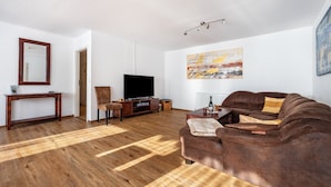 A living room with a wooden floor, a brown sofa, a TV, a coffee table, and a painting on the wall. - Holiday Apartment 5 with Private Terrace, Private Garden and Wi-Fi (Mardorf)