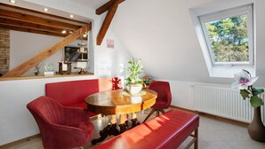 Un comedor con una mesa de madera, sillas rojas, un banco, una planta en maceta y una ventana con vistas a árboles.