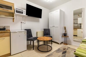 Une cuisine compacte équipée d’un micro-ondes encastré, d’un petit réfrigérateur et d’une table ronde en bois, accompagnée de chaises.