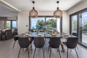 A modern dining area with a large table set for six, surrounded by black chairs, with a view of greenery and a clear sky through large windows. - Casa Calme With Spa And Gym, Opatija - Ičići, Croatia (Opatija - Ičići)