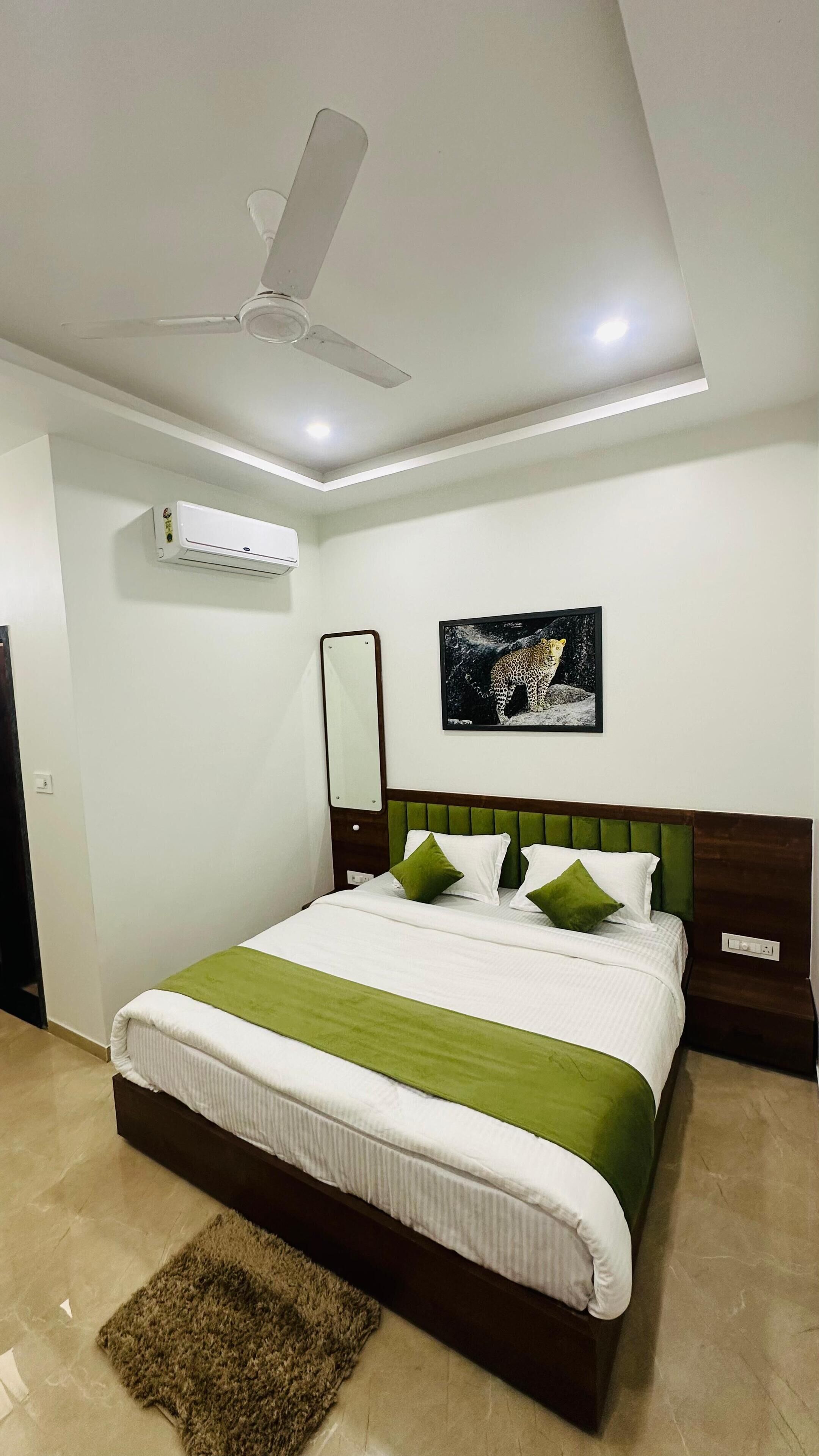 Camera da letto con un letto, una ventola a soffitto, un condizionatore, un quadro con un leopardo e una coperta da letto verde e bianca.