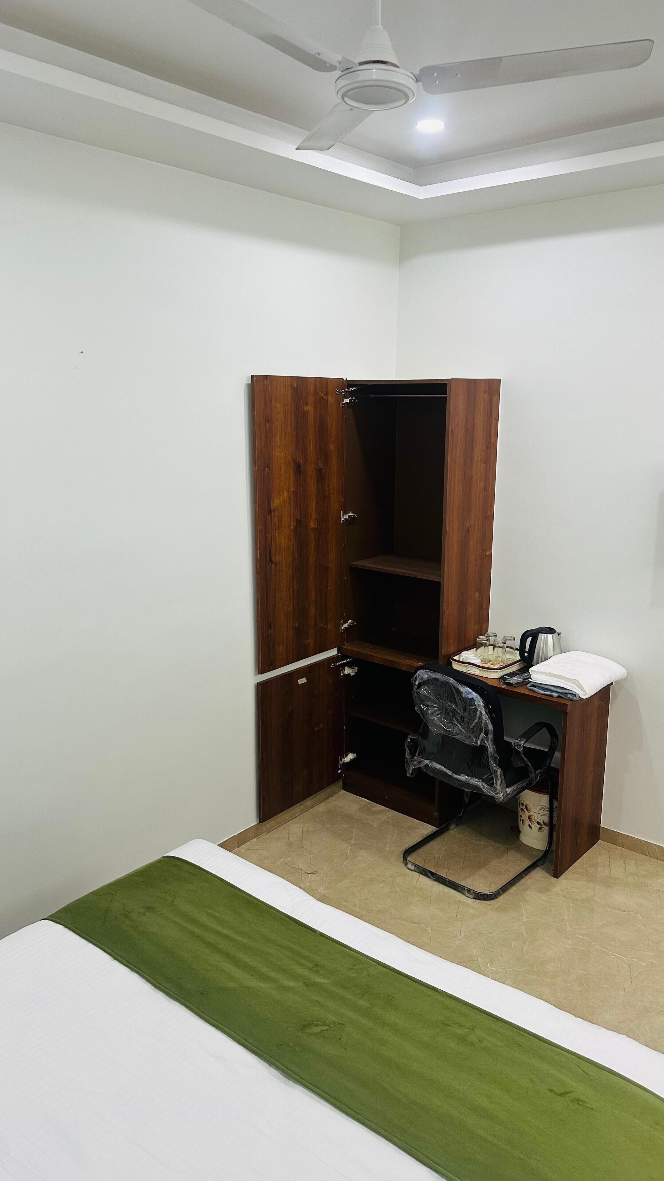 A bedroom with a bed, a desk, a chair, a wardrobe, and a ceiling fan.